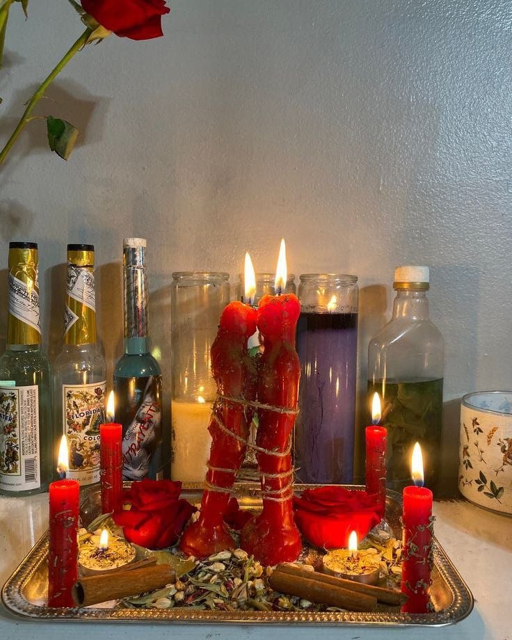 Red candles bound with cord, roses and herbs prepared on a tray for a love attraction spell